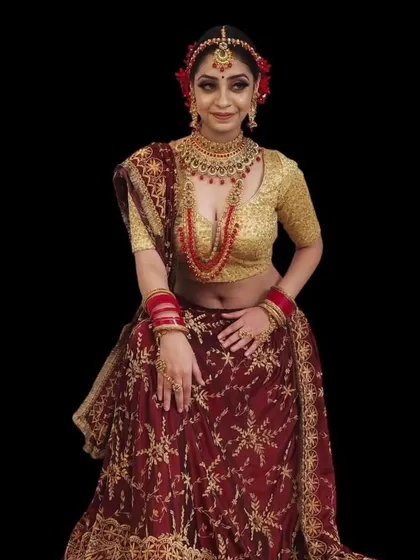 A bride in a traditional red and gold lehenga, wearing a layered red bead necklace.