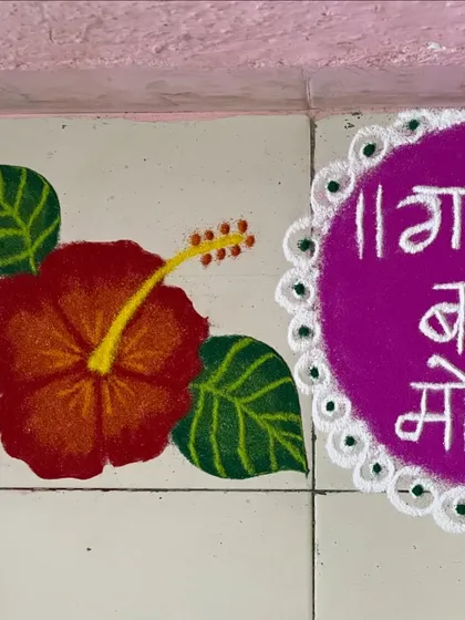 A rangoli for Ganesh Chaturthi, featuring the greeting "Ganpati Bappa Morya" in Marathi. The design is completed with a red hibiscus flower, which is traditionally offered to Lord Ganesha.