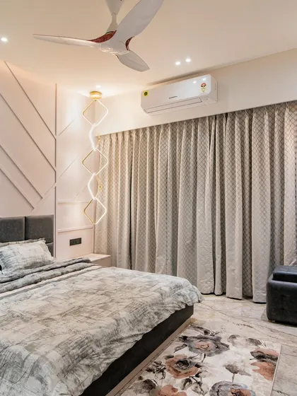 This bedroom design plays with texture and pattern, featuring a geometric paneled accent wall in a soft pink hue. A unique, winding LED light fixture acts as a piece of wall art.