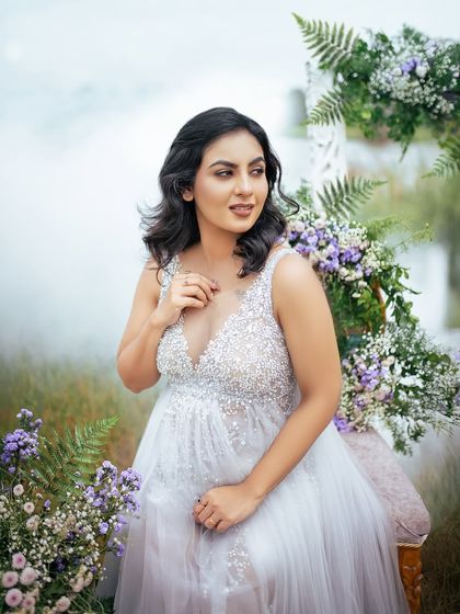 A close up portrait of the expectant mother, seated amidst a beautiful floral setup by the water. Her gentle expression radiates peace and happiness.
