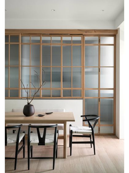 In this dining area, a white oak table is paired with black open-grain wishbone chairs. Versatile wooden sliding doors with fluted glass create a perfect harmony between an open and closed kitchen experience.