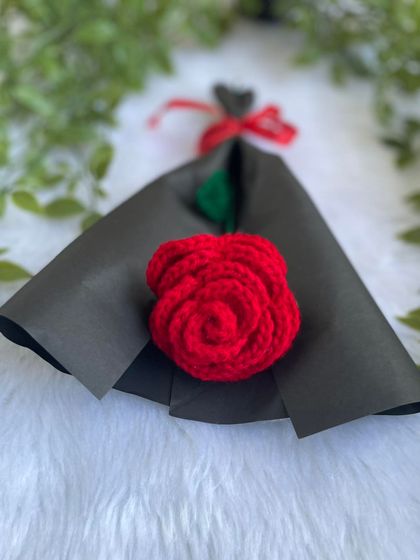 A single red crochet rose in its black wrapping, lying flat. The simplicity of the design makes it very elegant.