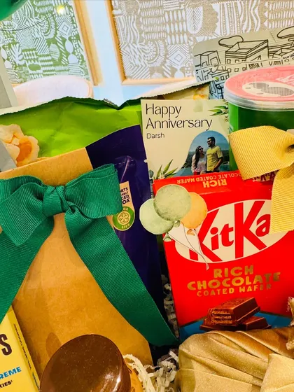 The hamper is a mix of textures and tastes, with KitKat bars, chips, and elegantly wrapped gifts tied with green ribbon.