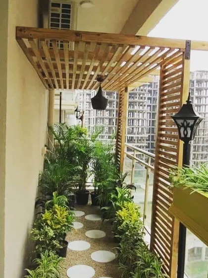This long balcony is designed as a green walkway. I installed a slatted wooden pergola overhead, a stone-pebble path, and filled the space with a variety of potted plants to create the feeling of a garden path with a city view.