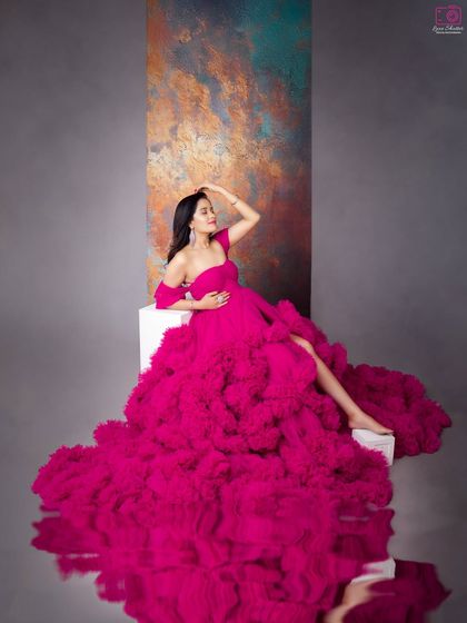 A confident and powerful pose. The combination of the bold magenta gown, the artistic backdrop, and the water reflection creates a truly unique and high-fashion maternity portrait.