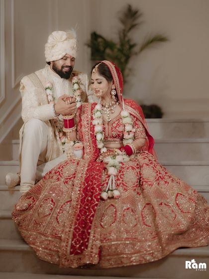 A beautiful portrait of the newly married couple seated on a staircase. The bride's magnificent lehenga is on full display, and the groom's gentle gesture towards her creates a sweet, candid moment.