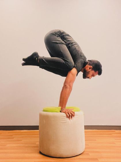 An elevated Crow Pose (Bakasana) on a prop. This increases the challenge and requires more core control to maintain balance.