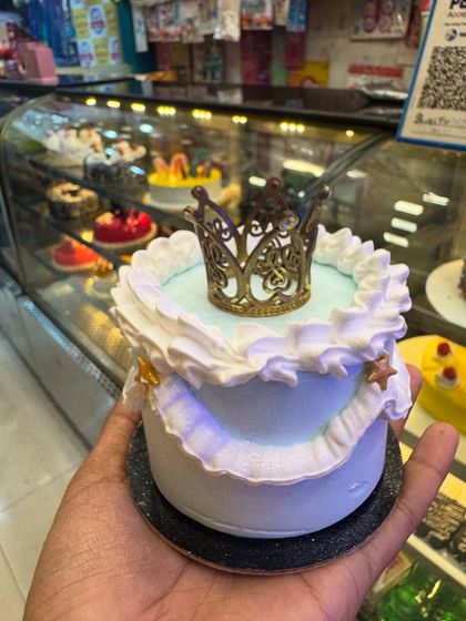 A royal mini cake with a delicate golden crown on top. The light blue color and frilly white piping give it a regal and charming look, perfect for celebrating your little prince or princess.