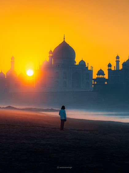 A lone figure stands on the banks of the Yamuna, watching the sunrise behind the Taj Mahal. This shot adds a human element and a sense of scale to the iconic monument.