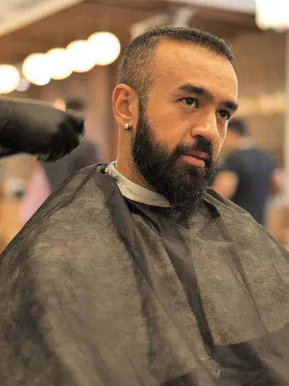 A close-up of a client in the barber's chair, ready for a haircut and beard trim. We cater to all men's grooming needs.