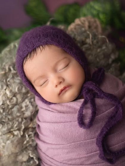 This little doll is nestled in a basket with lush greenery. The contrast between the soft purple wrap and the vibrant leaves is simply stunning.