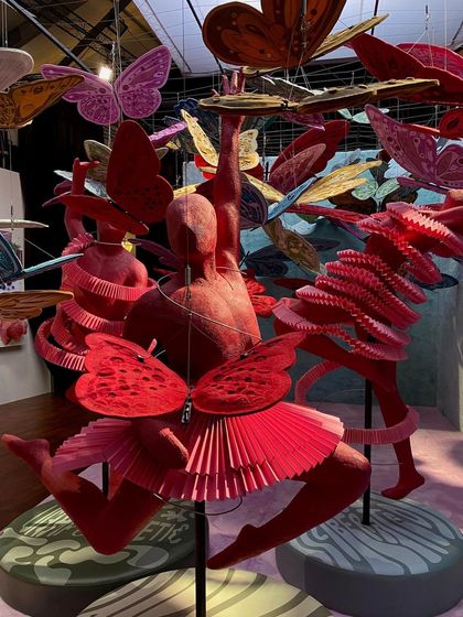 The 'We/Us' installation features multiple dancing figures in a cloud of butterflies. The entire scene is a dynamic and bold expression of liberation, confidence, and the joy of uninhibited movement.