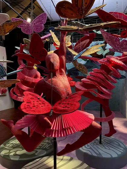 The full scene of the 'We/Us' installation, with multiple red dancer figures and a sky full of colorful butterflies. The entire piece is an explosion of adventurous energy and form.