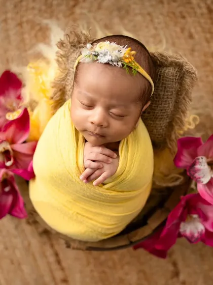 Bright and beautiful! This baby girl is wrapped in a sunny yellow swaddle, surrounded by vibrant magenta orchids for a colorful and cheerful newborn portrait.
