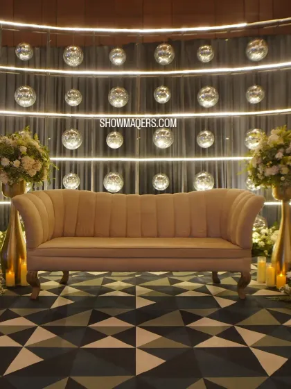 A chic photo booth for a ring ceremony, featuring a modern sofa against a backdrop of shimmering disco balls and soft white florals.
