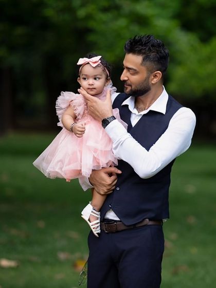 A father holds his daughter tenderly during their outdoor family photoshoot. The natural green background provides a beautiful, soft setting.