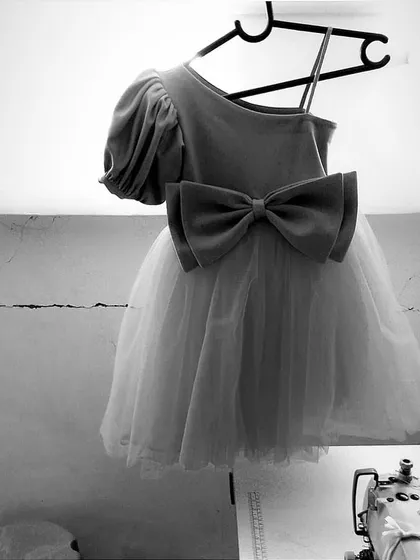 A glimpse of our creative process. This black and white photo shows a custom party dress with a large bow and puff sleeve hanging in our workshop, ready for the final touches.