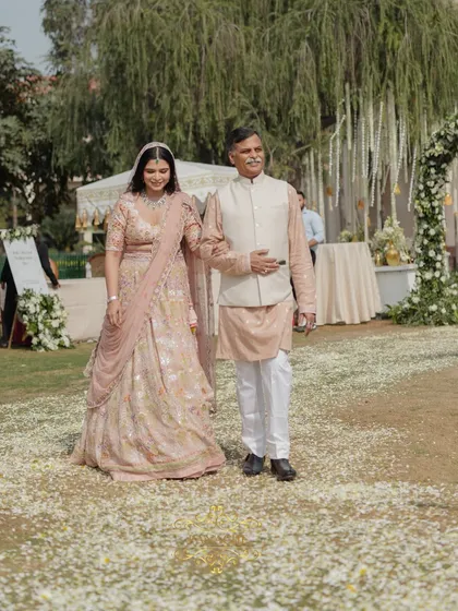 The bride and her father walk across a path scattered with flower petals, adding to the romance of the moment.