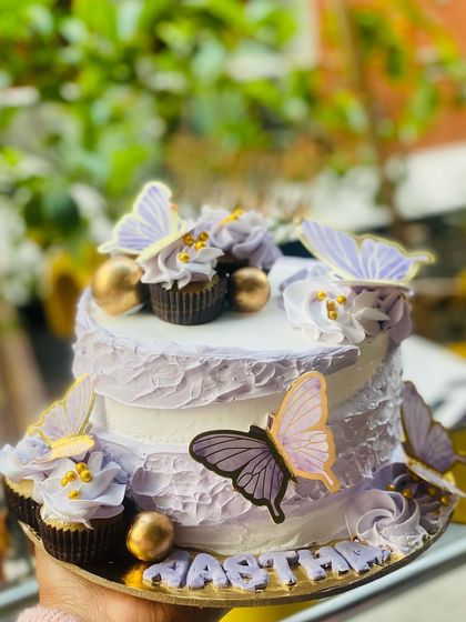 A beautiful lavender cake with butterflies and cupcakes on top.
