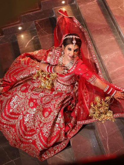 A beautiful top-angle shot showcasing the full spread of the bride's incredibly detailed red lehenga. Her pose exudes grace and confidence on her special day.