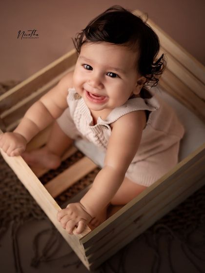 A happy baby boy peeking out of a wooden crate.