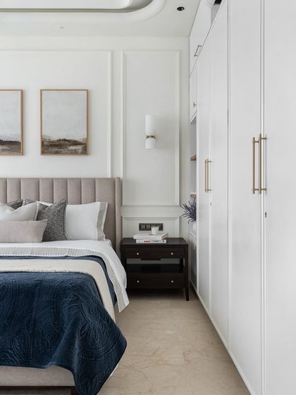 Neutrals are always in style. This bedroom showcases a calm and collected design with its soft grey headboard, crisp white wardrobes, and subtle wall mouldings, creating a timeless and elegant space.