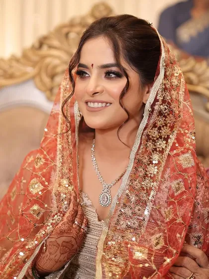 A beautiful, soft look for an engagement ceremony. The bride is wearing a delicate dupatta over her head, and her makeup is kept minimal and radiant, with a focus on her smiling eyes.