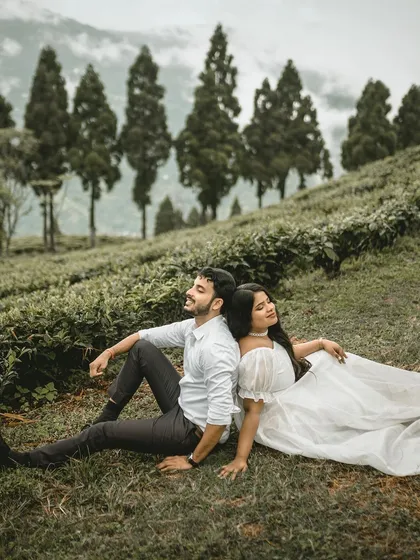 A serene moment of a couple resting back-to-back in a field. This pose is relaxed and symbolic, showing them supporting each other amidst the beautiful Darjeeling scenery.