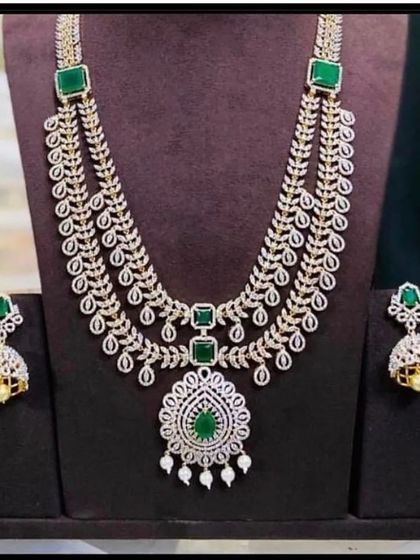 A beautiful layered necklace set with leaf-patterned chains and green stone accents. The matching jhumkas complete this elegant and modern look.