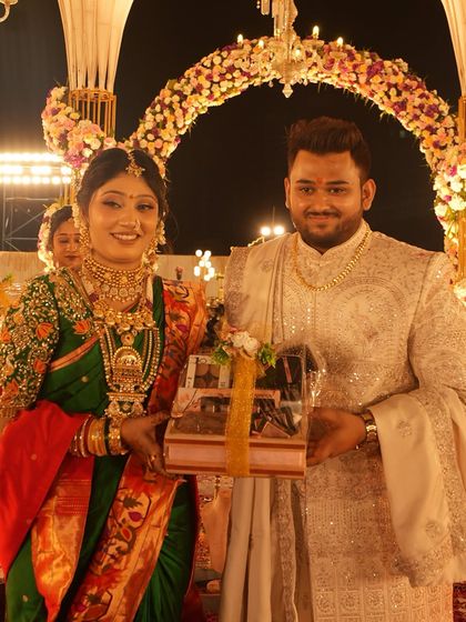 The couple sharing a happy moment at their reception. The bride's traditional green saree and the groom's elegant sherwani are complemented by the grand floral arch behind them.