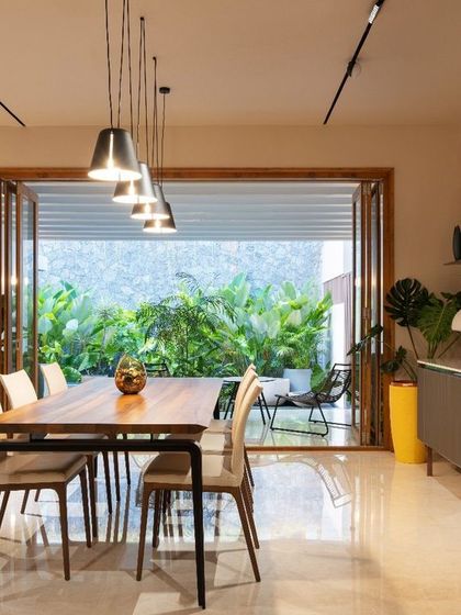 The dining room opens up completely to an outdoor patio, blurring the line between inside and out. Pendant lights hang over the dining table, while a geometric mirror wall adds a touch of artistic flair.