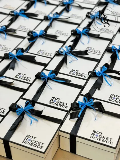 Custom gift boxes created for the brand "Not Rocket Science." The minimalist white boxes with the company's logo are paired with black and bright blue ribbons, perfectly matching their brand colors and modern aesthetic.