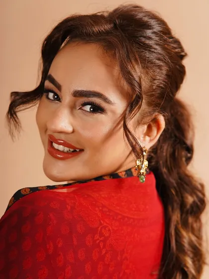 A bright and joyful look perfect for a festive celebration. The makeup features a glossy red orange lip, warm, defined eyes, and a playful, wavy ponytail that adds a touch of fun.