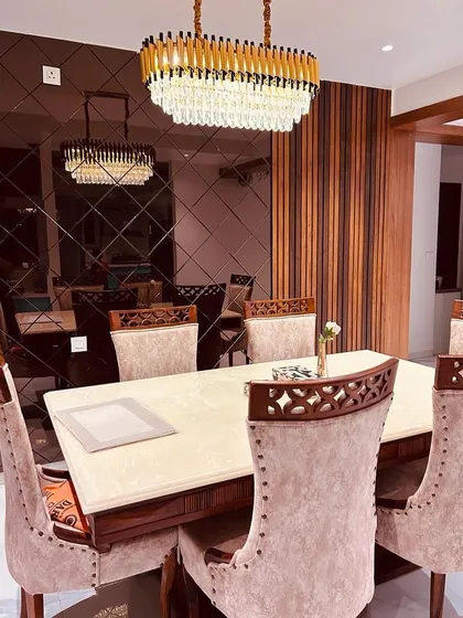 An elegant dining area designed for memorable gatherings. The space is defined by a stunning crystal chandelier, a reflective smoked-glass wall that enhances the sense of space, and luxurious upholstered chairs for ultimate comfort.