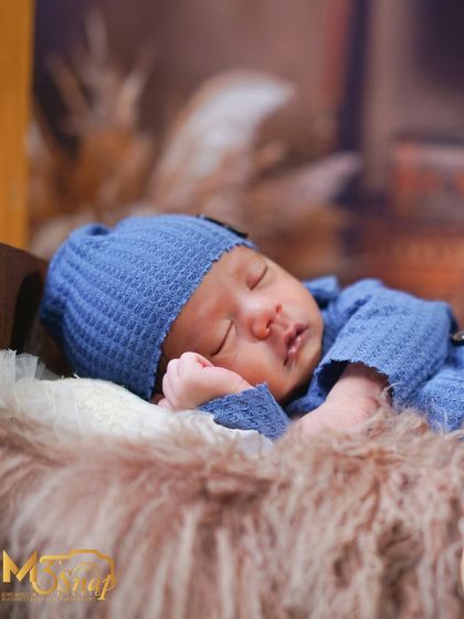 A peaceful shot of the newborn in a blue knit outfit, resting on a fur-lined tiny bed. The details in the outfit add a lovely texture.