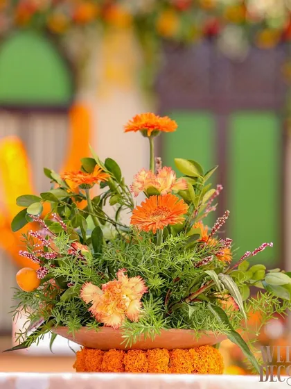 A simple yet beautiful centerpiece of orange gerberas and fresh greens in a terracotta bowl. Small details like this contribute to the overall thematic consistency.