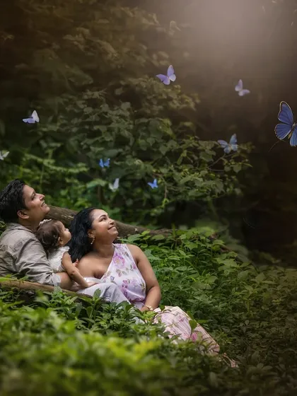 A duplicate of image 7, included for completeness. A family picnic with Mother Nature. This portrait captures a beautiful moment of connection as the family looks up at a swirl of blue butterflies in a dense, green forest.