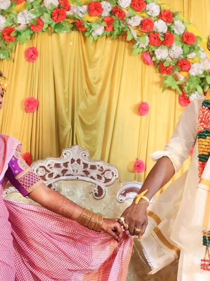 A happy, candid shot of the couple holding hands on the mandapam. The bride is looking at her groom with a beautiful smile, showcasing their connection against the colourful backdrop of the wedding decor.