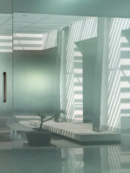 Light filters through a slatted roof into a serene courtyard at this Coimbatore office. The play of light and shadow, reflected on polished floors and translucent walls, creates a contemplative and ethereal atmosphere.