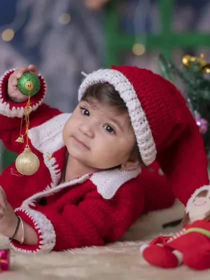 A tender moment from a Christmas session, with a baby in a Santa suit looking at a holiday ornament. The soft, warm lighting creates a cozy and magical atmosphere.