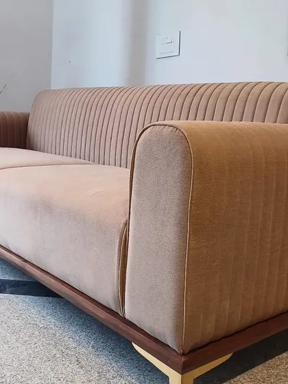 A modern three-seater sofa with channel-tufted back and arms, upholstered in a neutral beige fabric. The clean lines of the wooden base and legs give it a contemporary yet timeless appeal.