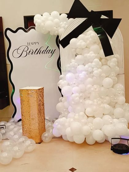 A chic black and white themed decoration with a unique, modern backdrop. The setup is softened by a cascade of white balloons and a large black bow.