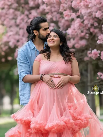 An outdoor maternity shoot in Bangalore's beautiful parks. The natural light and blooming pink flowers create a soft, romantic setting for this happy couple's pregnancy portrait.