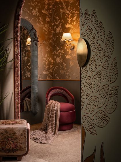 A glimpse into the romantic and detailed world of Zone Two. A custom-designed chair in a rich red velvet sits in a corner defined by floral wallpaper and a unique, fabric-wrapped archway, creating an intimate and immersive atmosphere.