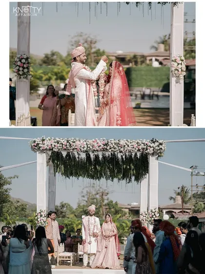 The varmala exchange at an outdoor daytime wedding. The bright sunlight and beautiful floral mandap create a fresh and vibrant setting for this key wedding moment.