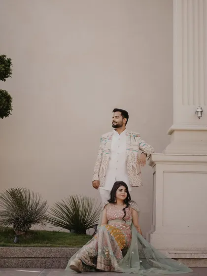 An elegant and poised portrait. The couple is posed against a grand pillar, creating a stately and classic image that showcases their beautiful pastel outfits.