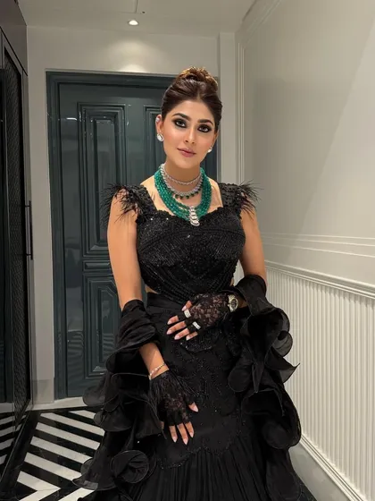 This high bun complements the dramatic silhouette of the black gown, creating a powerful and chic look for a formal evening event or reception party.