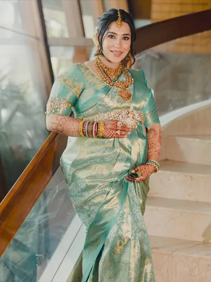 A full-length shot showcasing the bride's elegance. The soft makeup look works beautifully with the intricate gold jewelry and the shimmering silk saree.