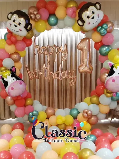 A jungle animal themed first birthday photo booth. The circular balloon arch is decorated with monkey and cow foil balloons.