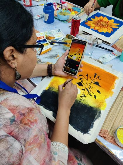 A doctor uses her phone as a reference to paint a stunning sunset on a tote bag during our special corporate workshop.
